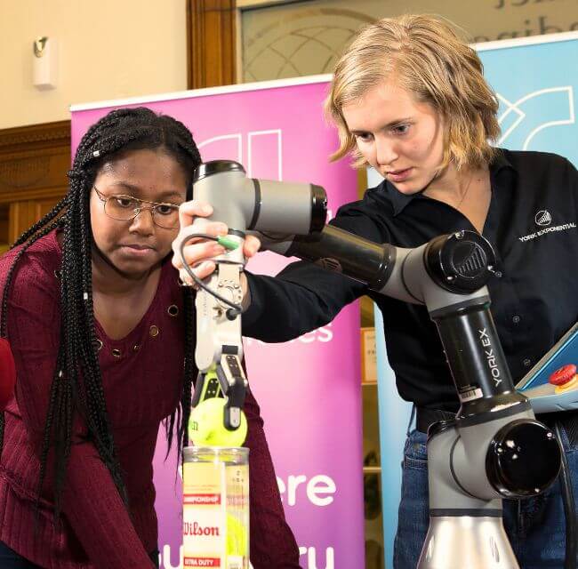 Two Teens Work With A Robotic Arm During A Library Program