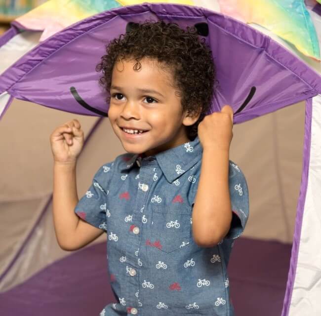 close up of little boy hiding under play tent smiling