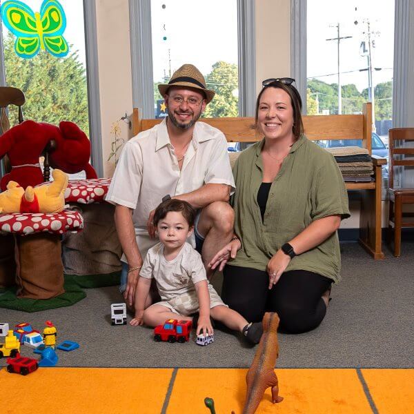 Family Of Three Sitting On Floor Smiling At Camera