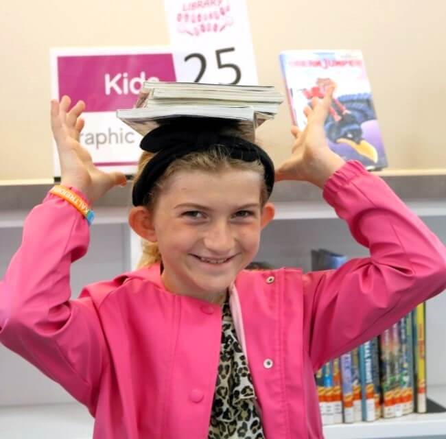 girl holding stack of books on top of head