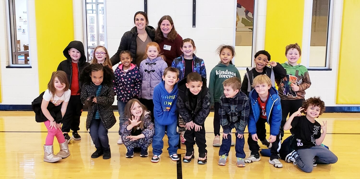 A group of smiling children and their teacher taking a commemorative picture with author Laura Gehl.