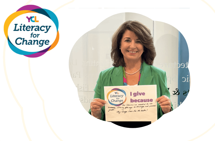 Photo of Jackie Summers holding a Literacy for Change sign that reads "I give because our libraries are essential to our community, offering gateways to knowledge and personal growth. They change lives for the better!"