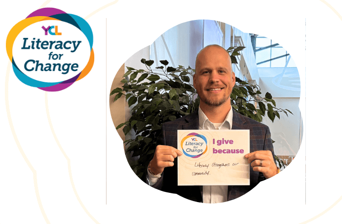Photo of Ricky Grey holding a Literacy for Change sign that reads "I give because Literacy strengthens our community."