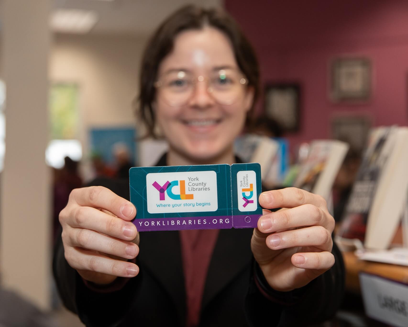 woman holding library card out to camera. Her face is blurred in the background